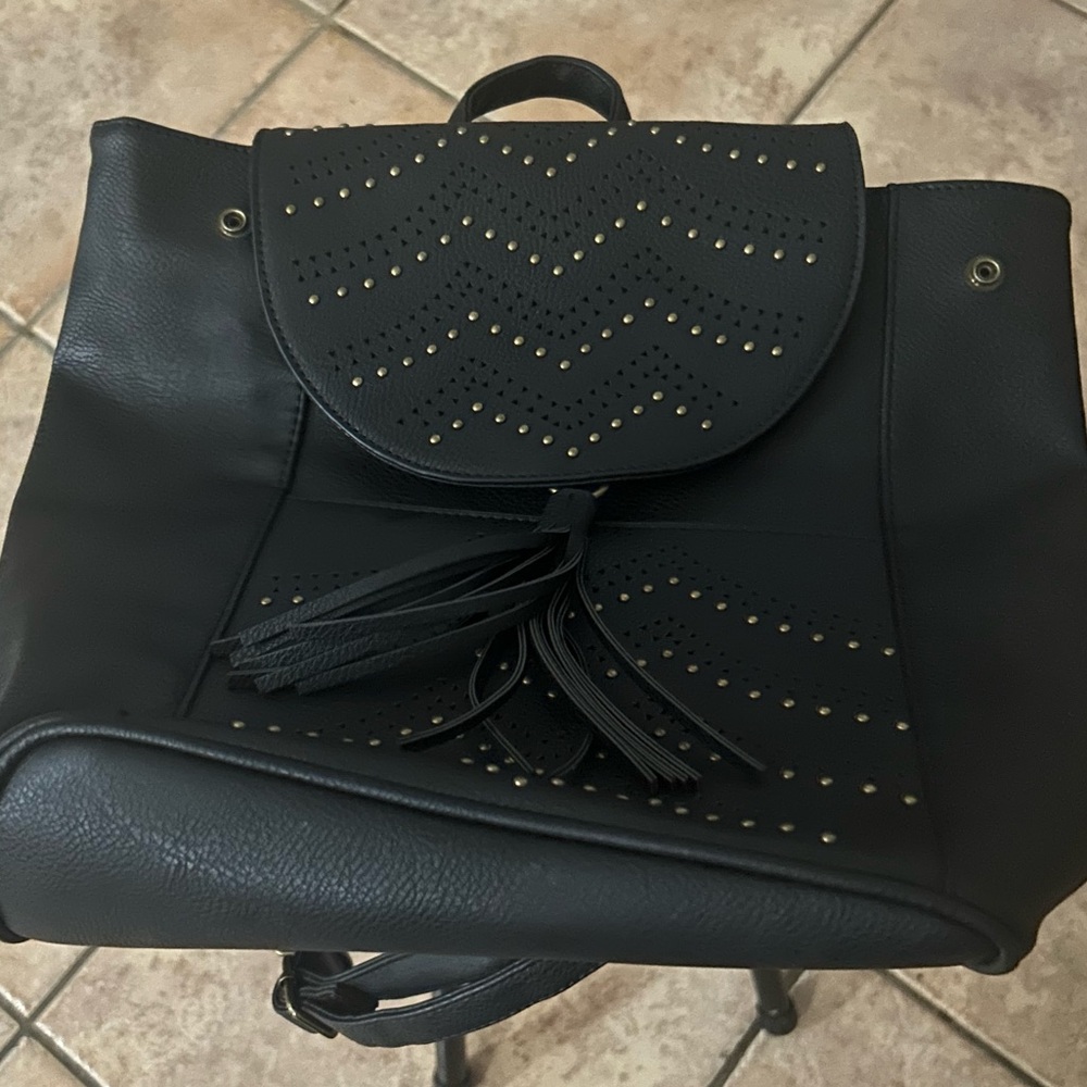 Black backpack with bronze studs, small bag on the back, yellow fabric inside.